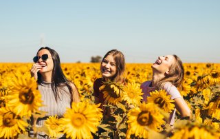 Three women smiling and standing in a field all of sunflowers