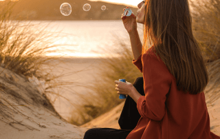 A woman sits on a sandy beach blowing bubbles