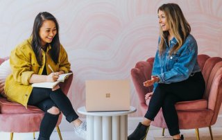 Two woman happily look at a laptop while one takes notes
