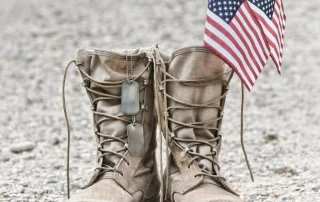 A solider's boots with dog tags and two American flags