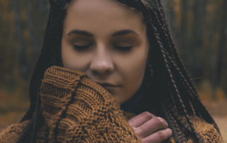 A woman in a fall forest closes her eyes