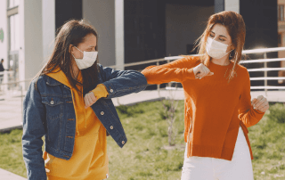 Two women bumped elbows while social distancing and wear masks