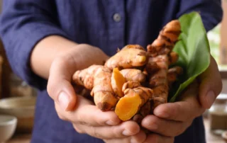 Open hand holding turmeric root and fresh herbs in soft morning light, representing plant-based wellness traditions.